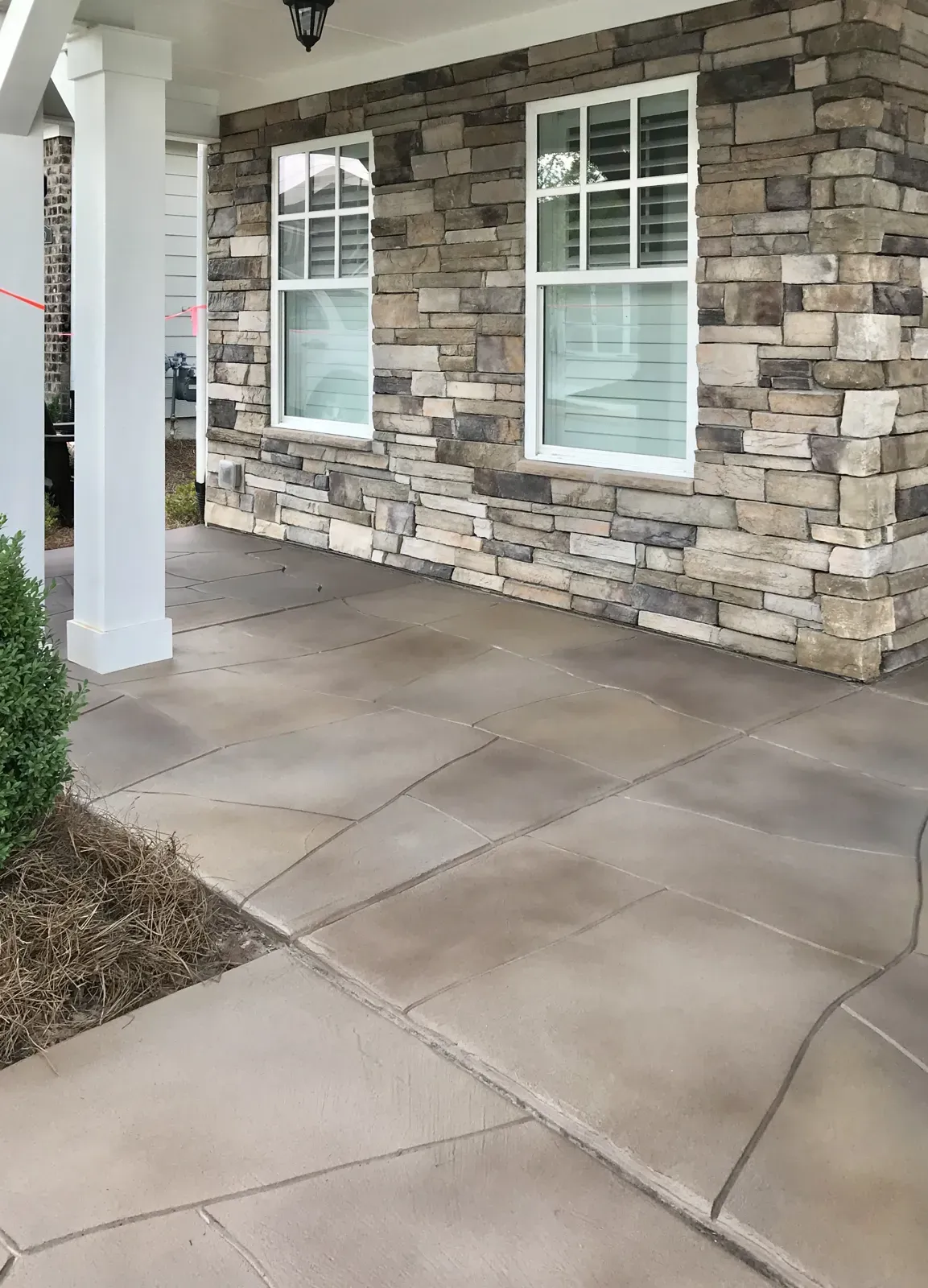 Front porch and walkway with a scored stone-look concrete finish beside stacked stone in Powder Springs GA